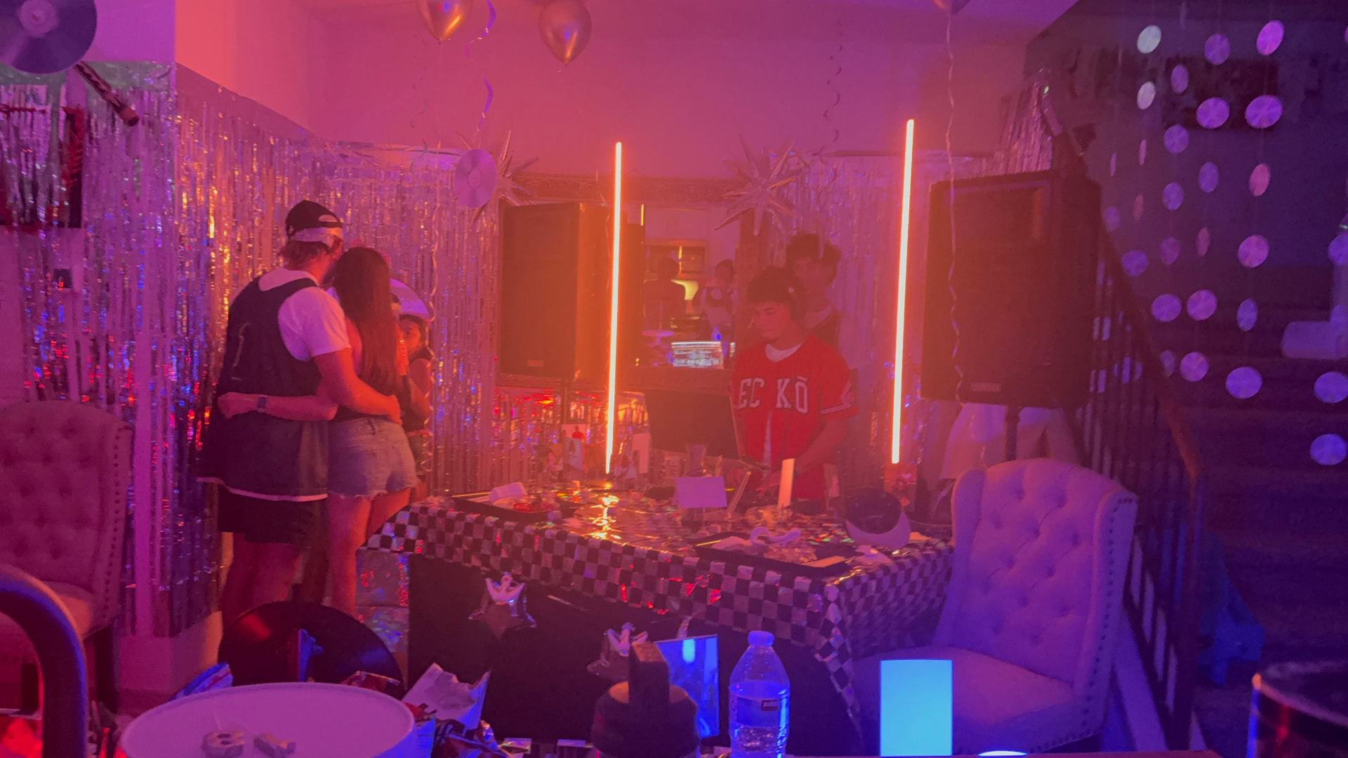 DJ Vinceanator at a house party with colorful neon lights, balloons, and guests